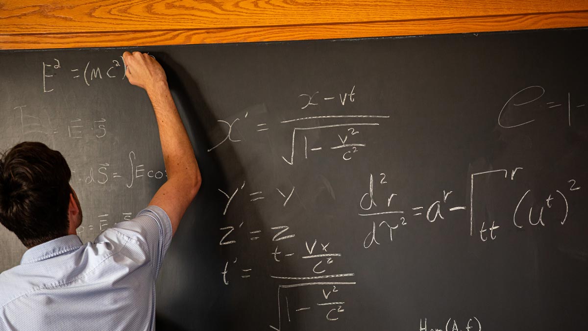 A student writes an equation on a chalkboard.
