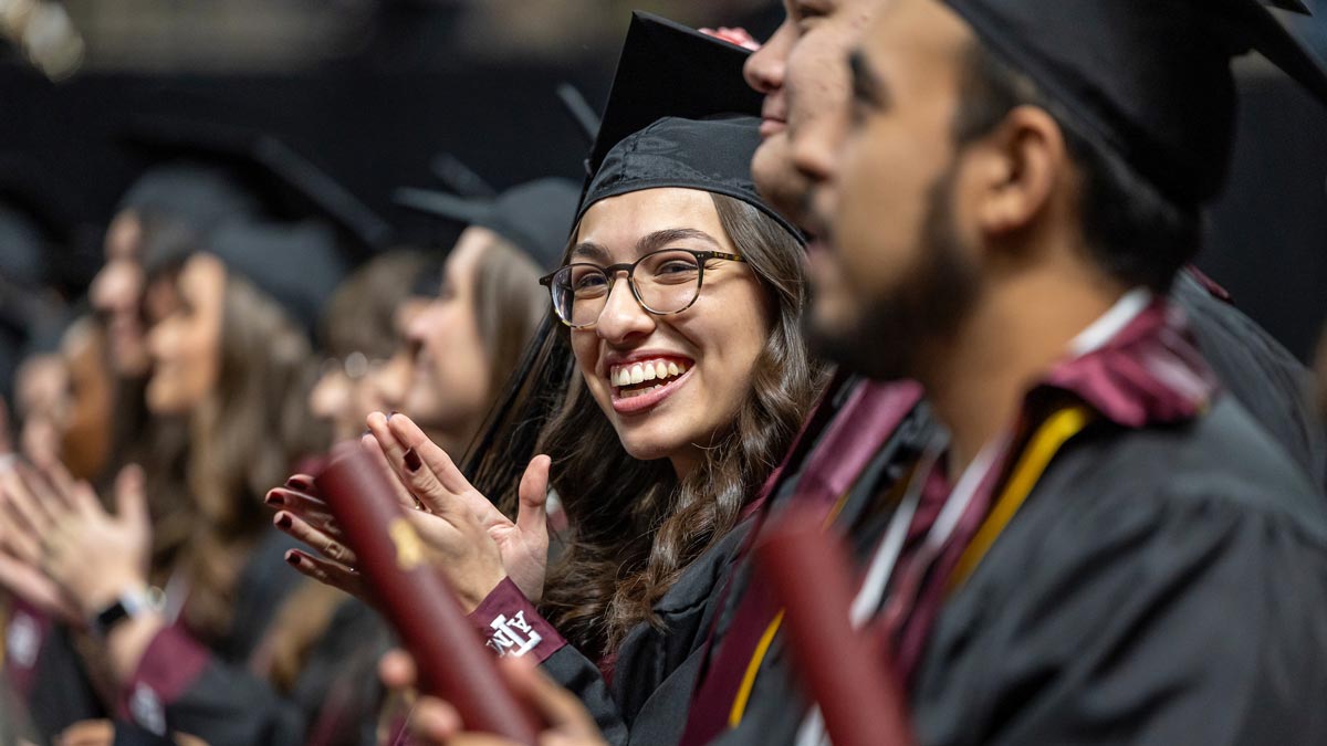 An Aggie graduate claps during her graduation ceremony.